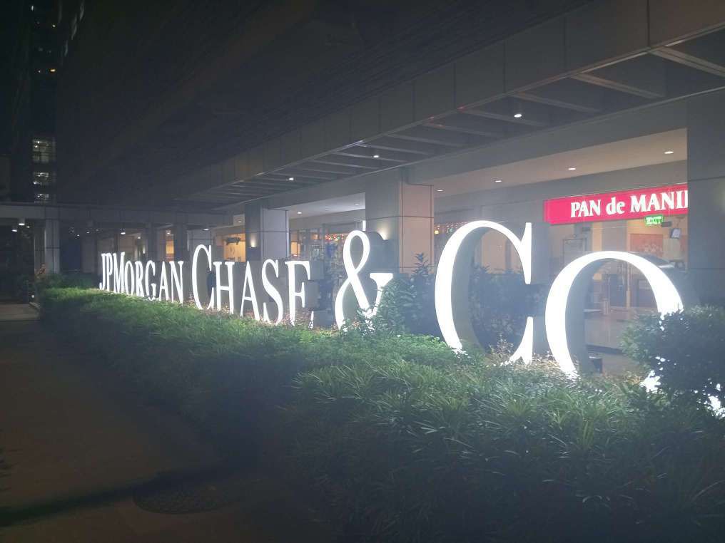 JPMorgan Chase and Co lit signage at night on top of trimmed plants located at the sidewalk.