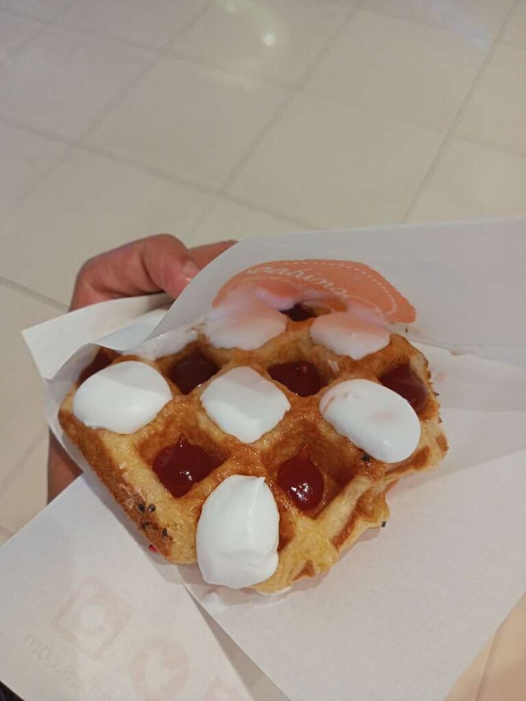 Belgian waffle in hand with cavities filled in red and juicy strawberry jam and white fluffy creme.