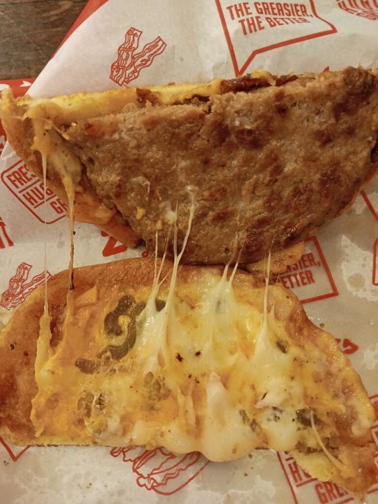 An open section of Zark's Grilled Cheeseburger showing the patty on the upperside and jalapeños swimming in melted cheddar cheese at the bottom.