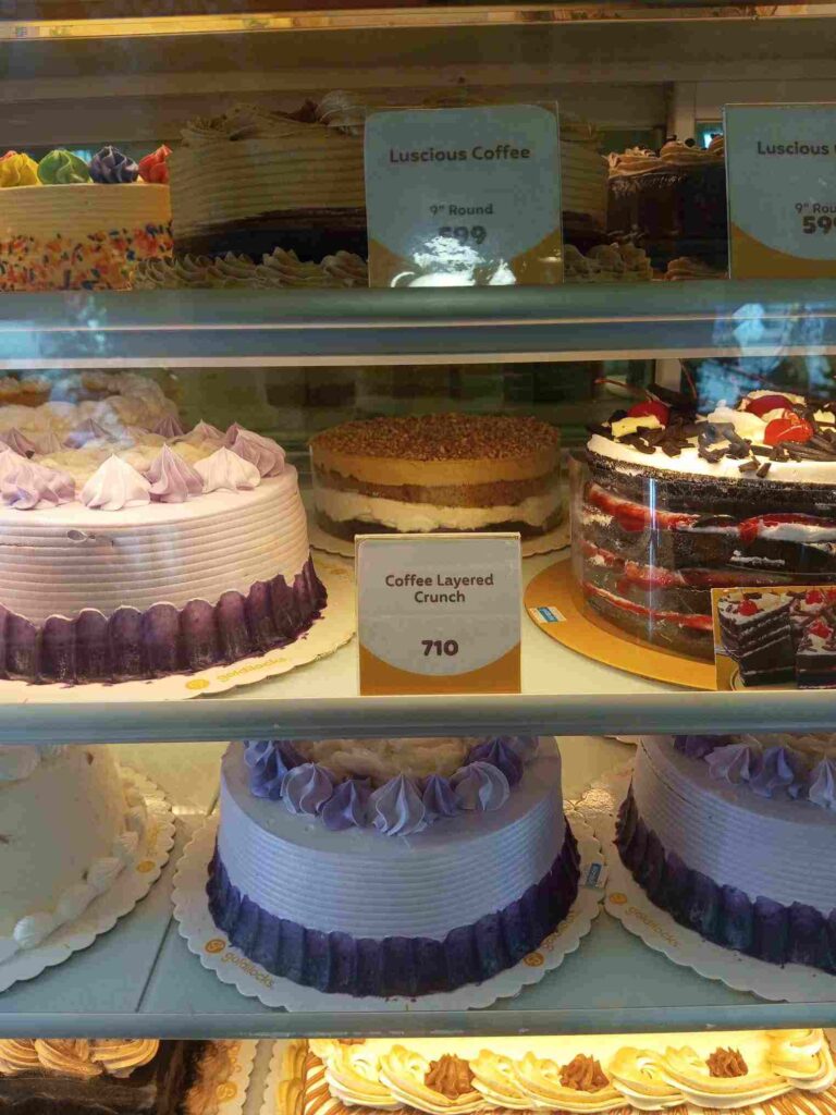Goldilocks Bakeshop cake displays featuring Coffee Layered Crunch and Luscious Coffee prices.