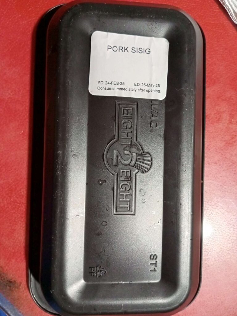 A black plastic container showing the back side that labels it's for a Pork Sisig meal. The brand of the container is embossed and reads as Eight 2 Eight.